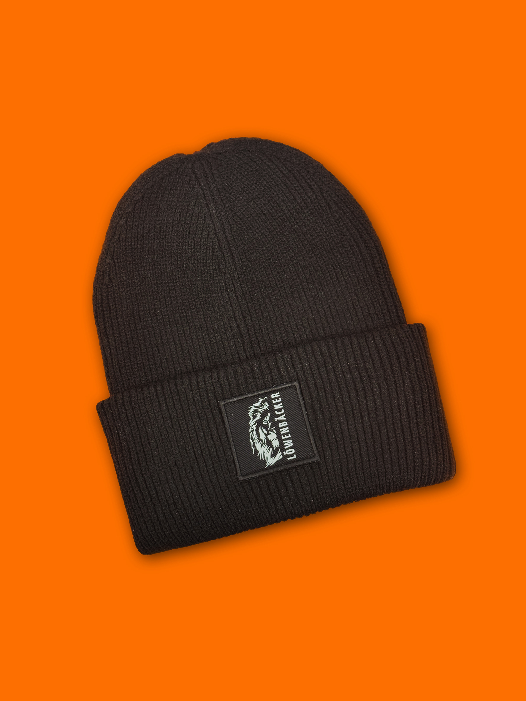 Eine schwarze Strickmütze mit Löwenlogo und Schriftzug auf leuchtend orangem Hintergrund