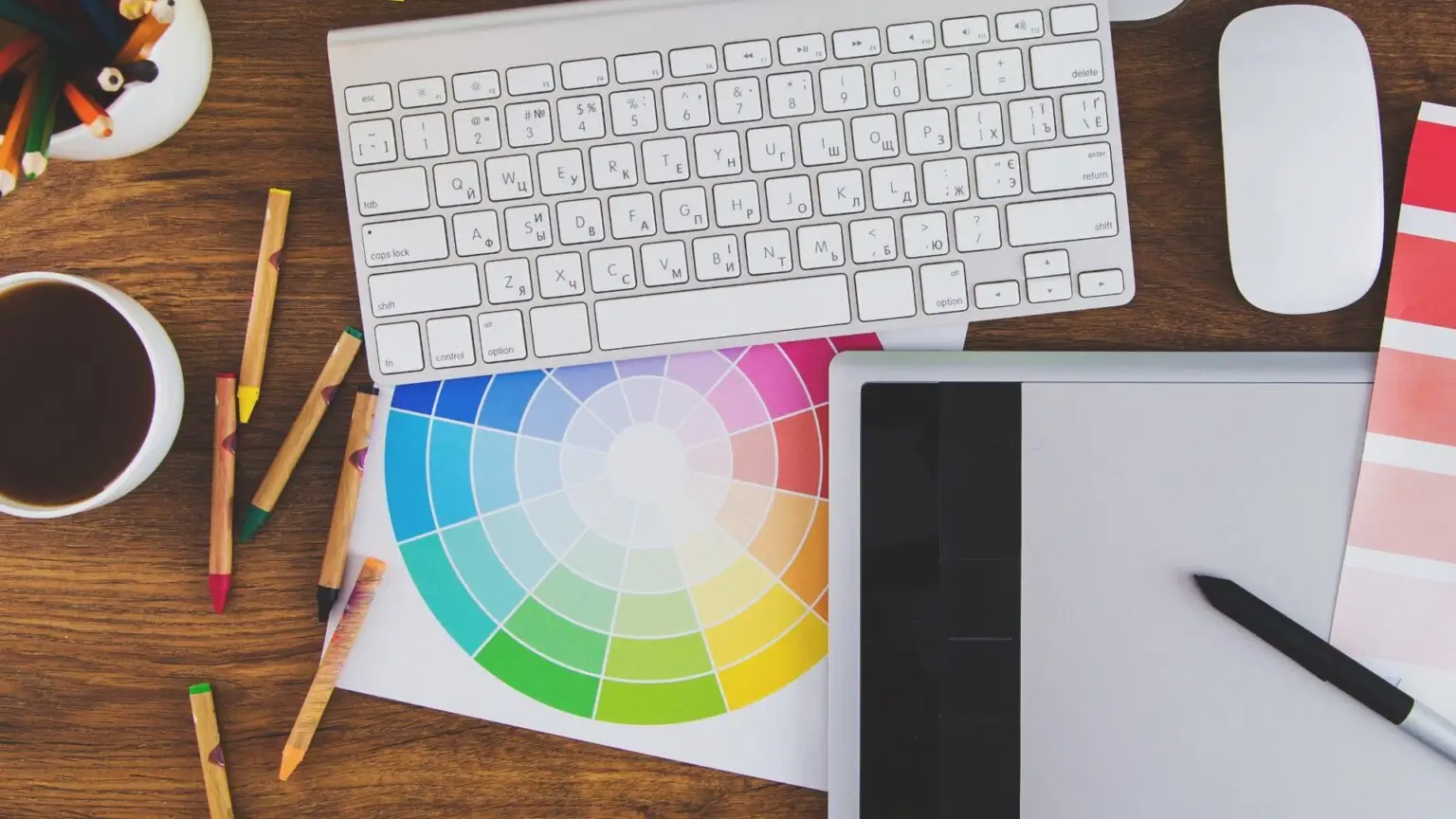 Eine moderne Tastatur, ein Grafiktablet und ein bunter Farbkreis auf Holztisch