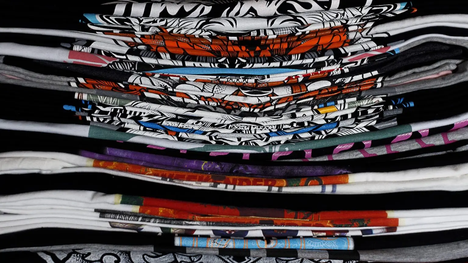Mehrere bunte, ordentlich gefaltete T-Shirts mit auffälligen Mustern und Drucken