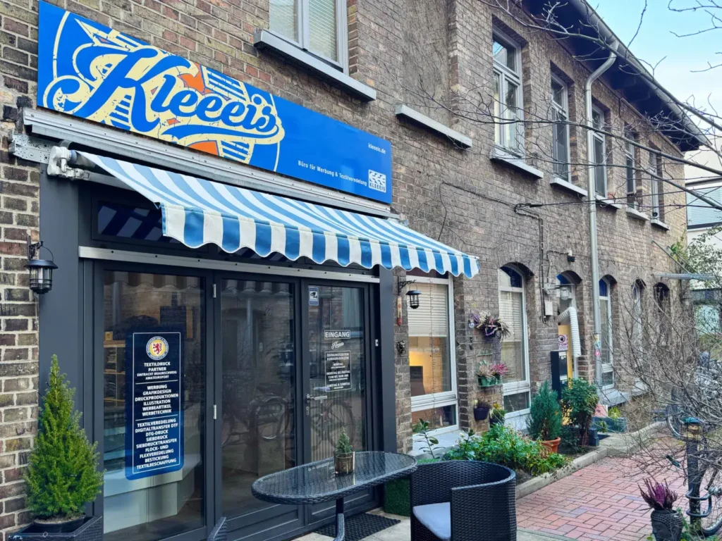 Eingang zu Kleeels mit blauweisser Markise an Backsteinfassade