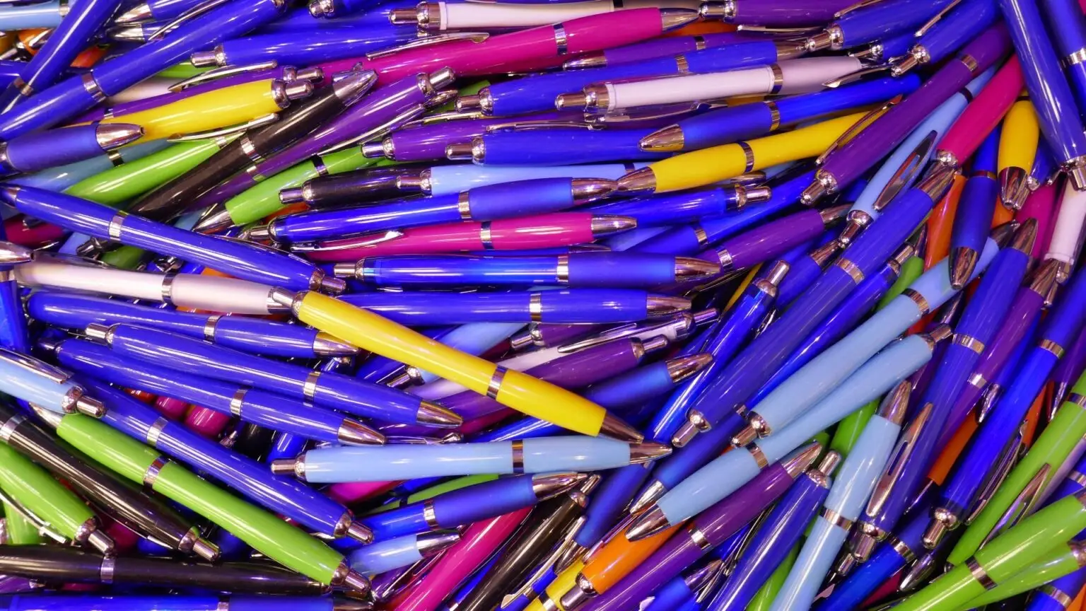 Viele bunte Kugelschreiber ohne Gesicht, glänzend, in Blau, Grün und Pink gestapelt
