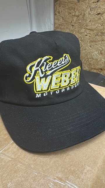 Schwarze Kappe mit gelber Weber Motorsport Stickerei auf einem Karton