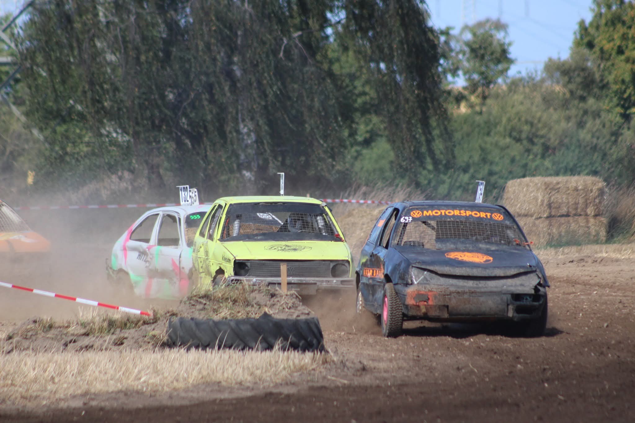 Drei Autocross Rennwagen in Weiss Gelb und Schwarz kaempfen im Staub um die Kurve