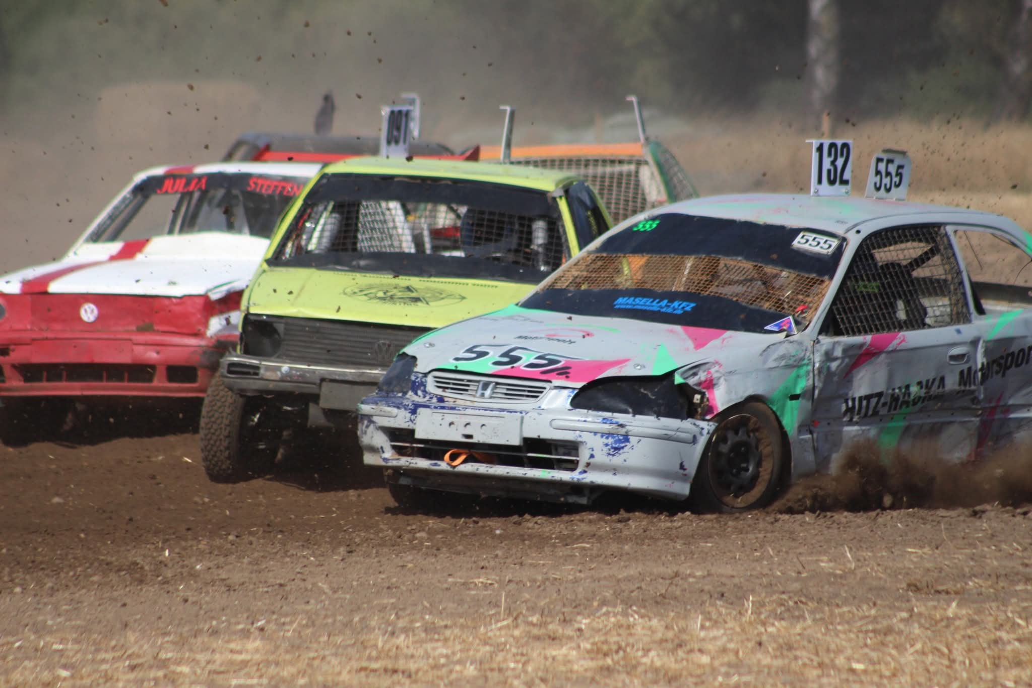Drei ramponierte Stockcar Rennwagen kaempfen auf staubiger Bahn um die Fuehrung