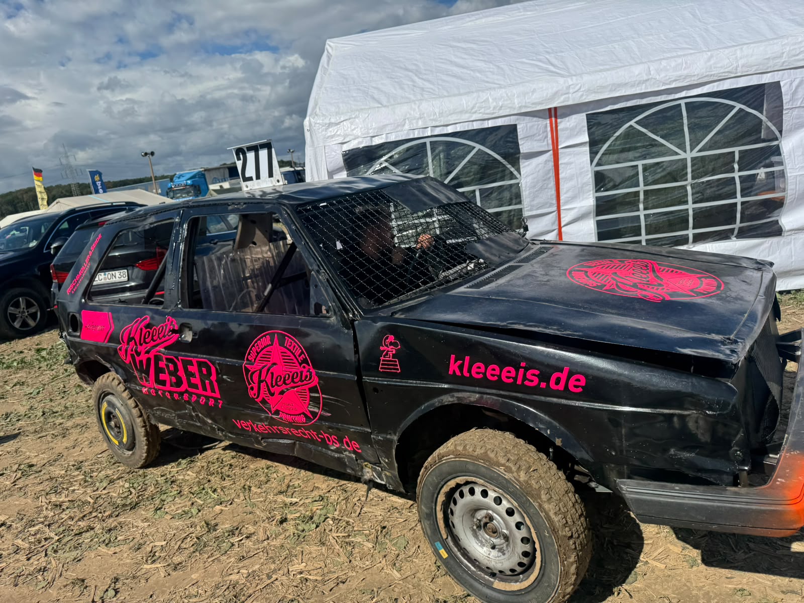 Schwarzes Stock Car mit pinken Aufklebern und Gitter vor weissem Zelt