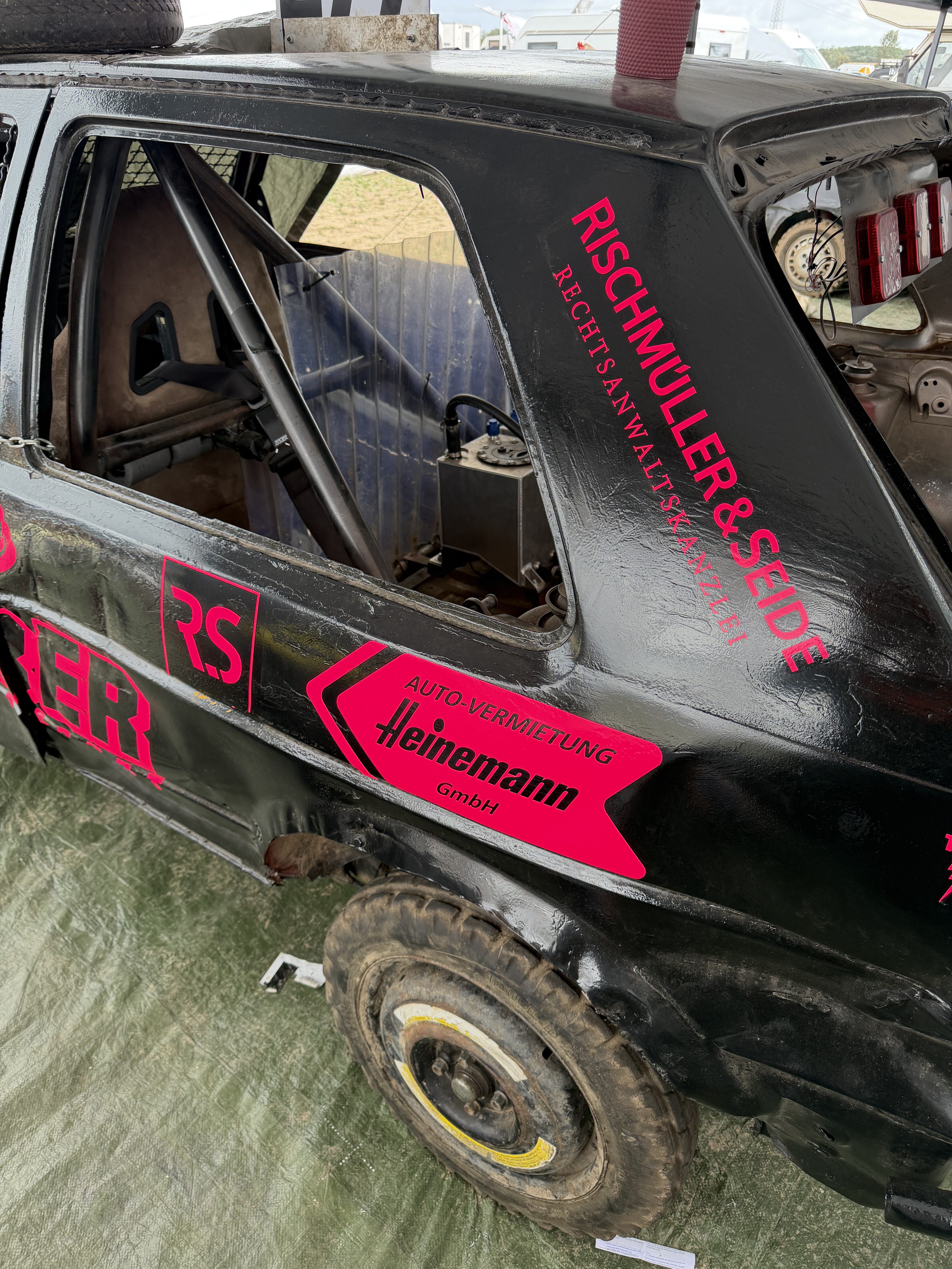 Schwarzes Stock Car Rennfahrzeug mit pinken Sponsorenaufklebern und Ueberrollkaefig