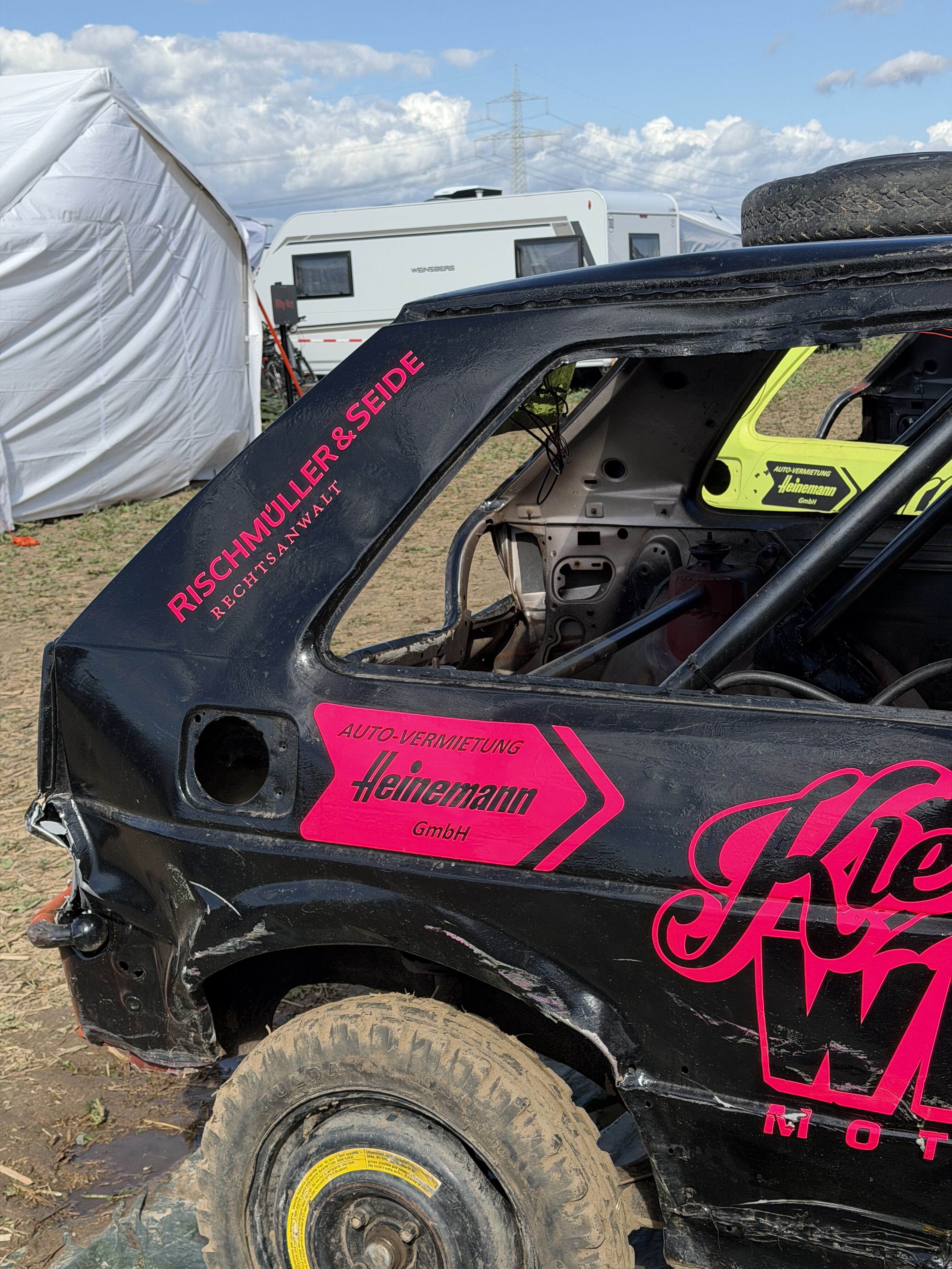 Schwarzes Stock Car mit pinken Sponsoraufklebern vor einem Wohnwagen