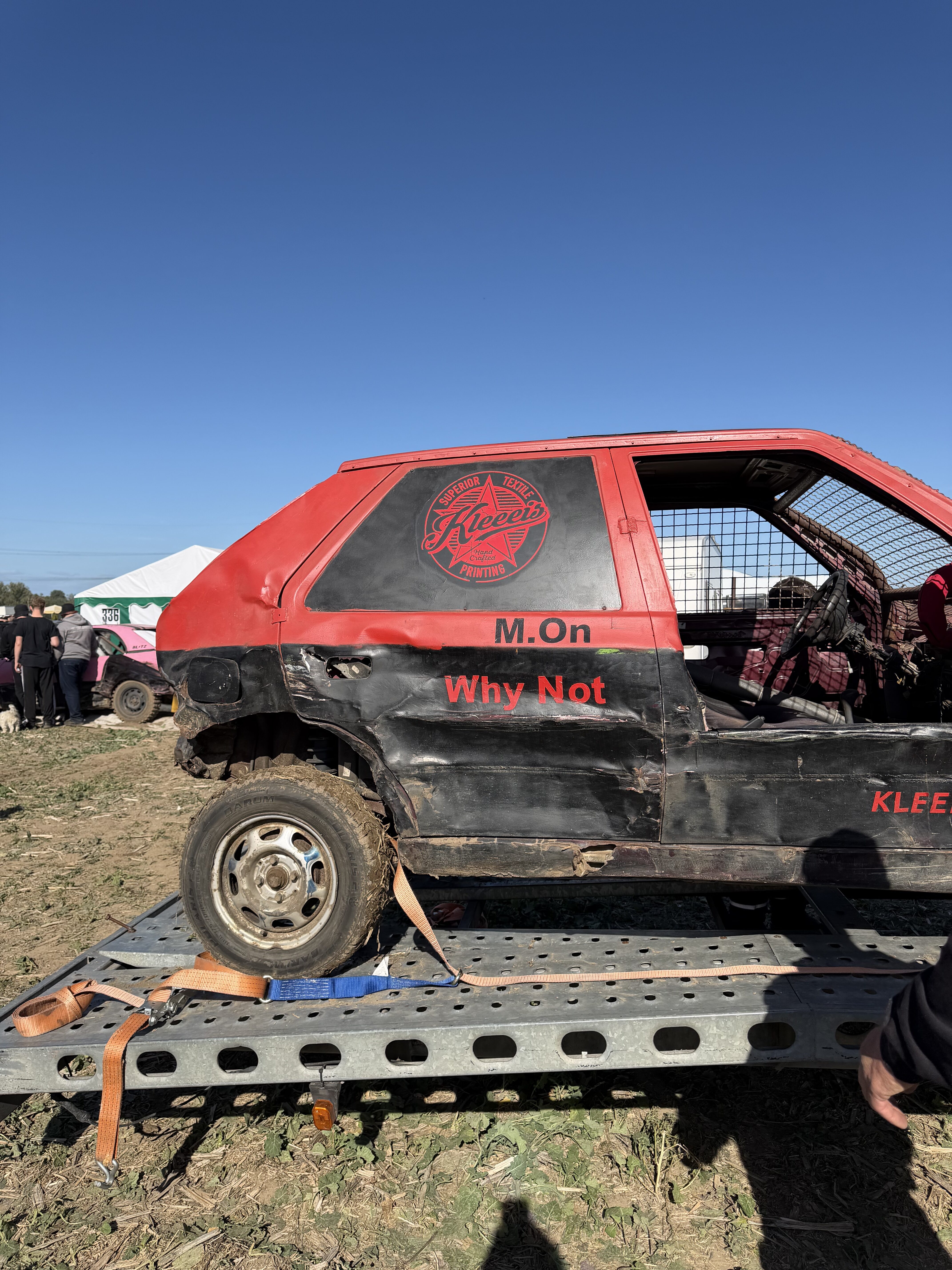 Ein rot schwarzes ramponiertes Stock Car mit Aufschrift Why Not auf einem Anhaenger