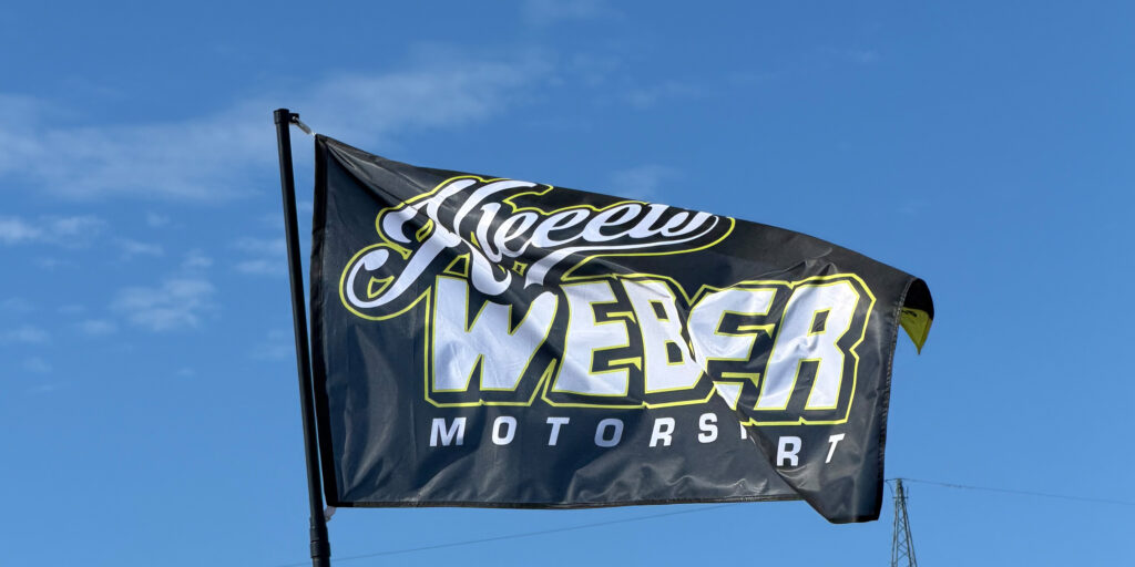 Schwarze Weber Motorsport Flagge weht im Wind vor blauem Himmel