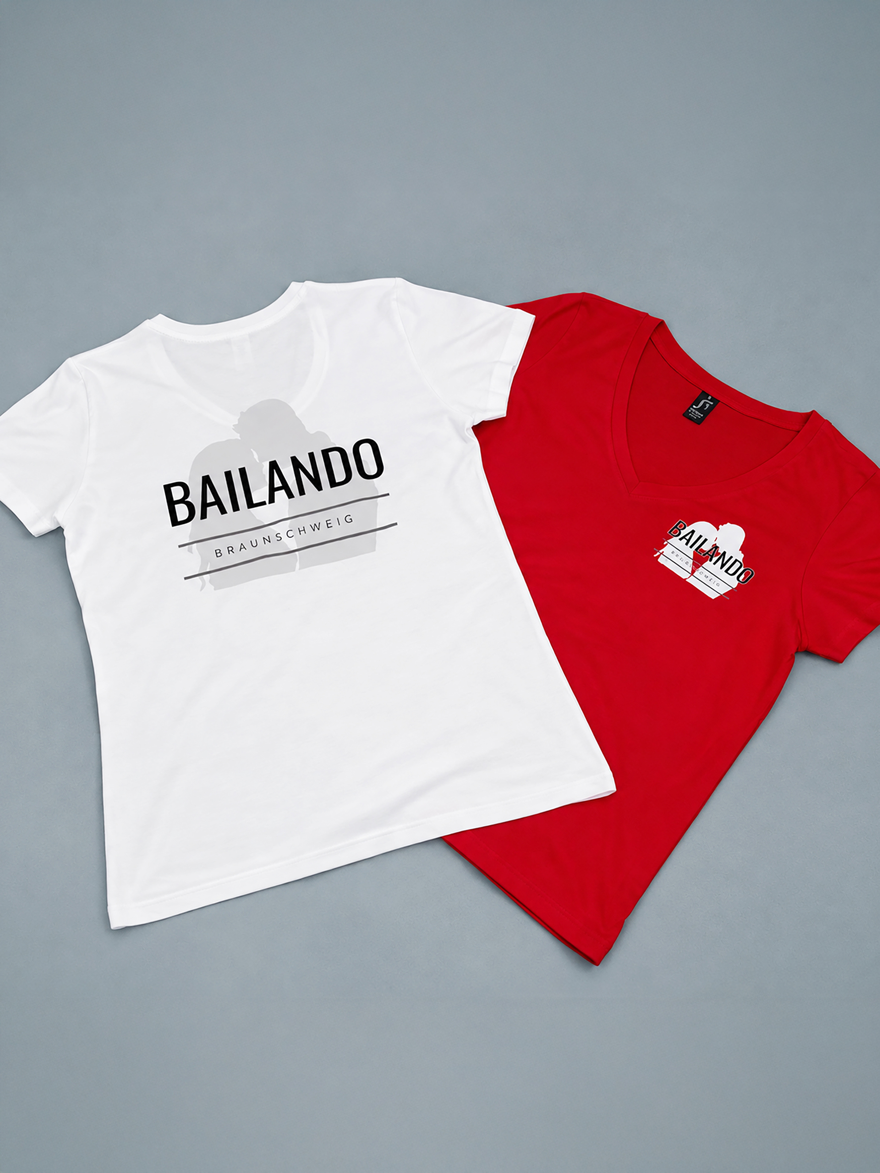 Zwei T-Shirts in Weiss und Rot mit Bailando Braunschweig Aufdruck auf grauem Grund