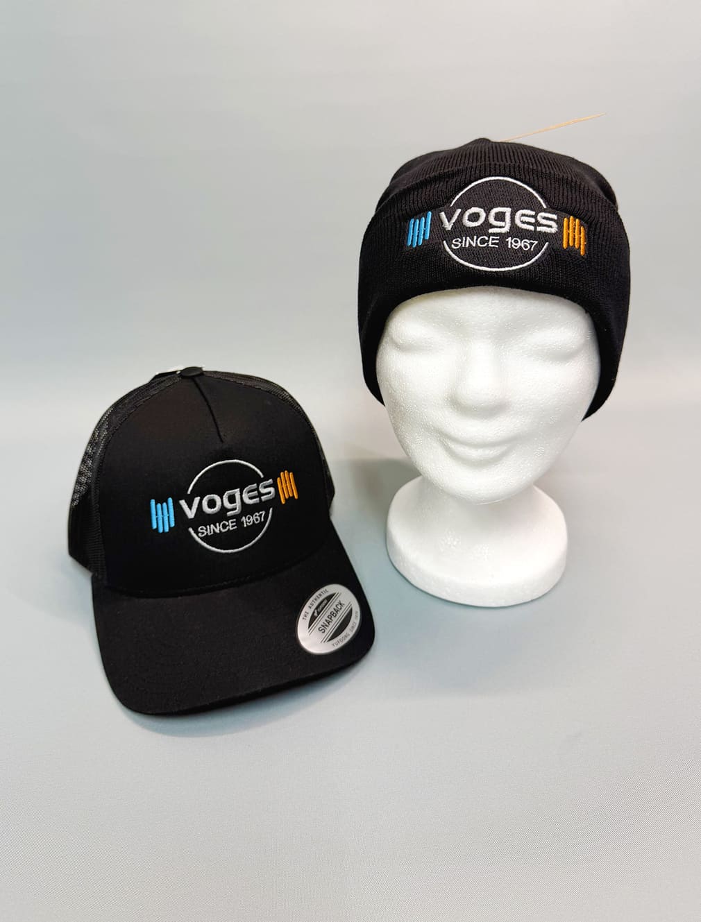 Schwarze Muetze und Cap mit Voges Logo auf weissem Styroporkopf